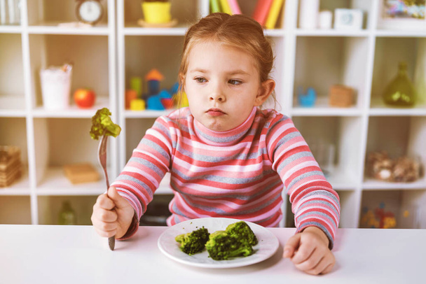 Vicces kislány brokkolit eszik villával. - Fotó, kép