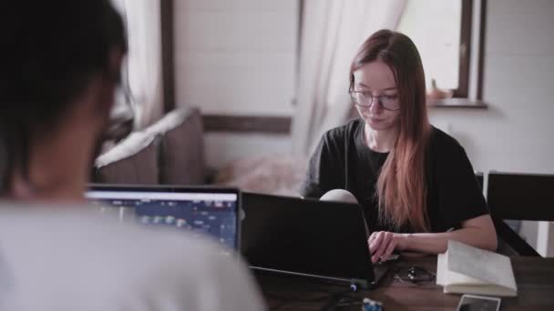 A young man and a young girl are working in front of laptops in their bright apartment. Work from home during the quarantine. Remote work of freelancers. Beautiful young pensive girl in glasses in front of a computer monitor. - Footage, Video