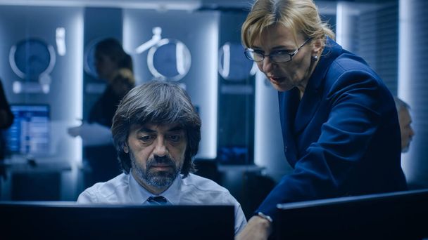 Female Manager Talks with Professional Operator Working on a Personal Computer in the System Monitoring Room. High Profile Specialist Working. - Φωτογραφία, εικόνα