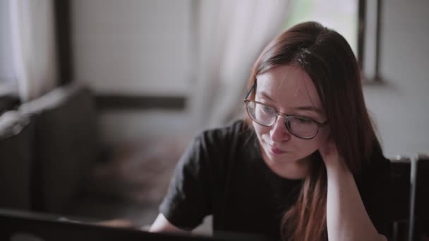 Egy fiatal férfi és egy fiatal lány laptopok előtt dolgoznak a fényes lakásukban. Dolgozz otthonról a karantén alatt. Szabadúszók távoli munkája. Gyönyörű fiatal gondolkodó lány szemüvegben egy számítógép monitor előtt. - Felvétel, videó