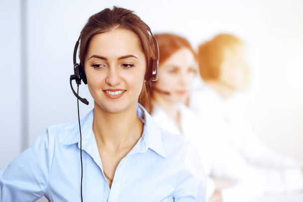 Operadores del centro de llamadas. Céntrate en la hermosa mujer de negocios usando auriculares en la oficina soleada - Foto, imagen