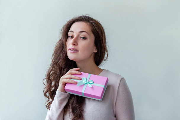 Young positive woman holding small pink gift box isolated on white background. Preparation for holiday. Girl looking happy and excited. Christmas birthday valentine celebration present concept - Foto, immagini