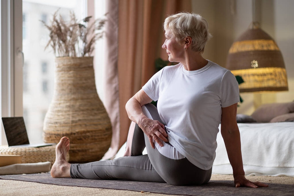 Senior caucasian woman in half spinal twist pose on mat - Photo, Image
