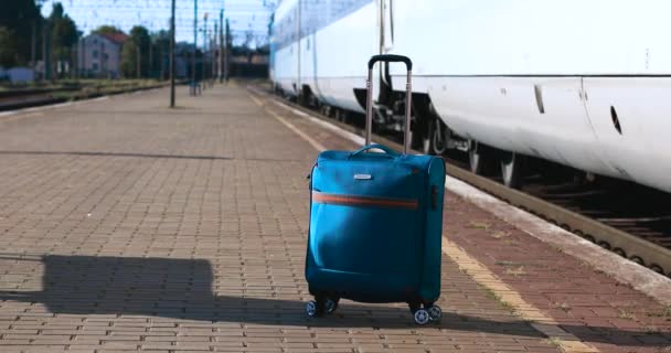 A vasútállomáson egy kék bőrönd áll. A nagysebességű vonat indul a peronról. Utazási és nyaralási koncepció - Felvétel, videó