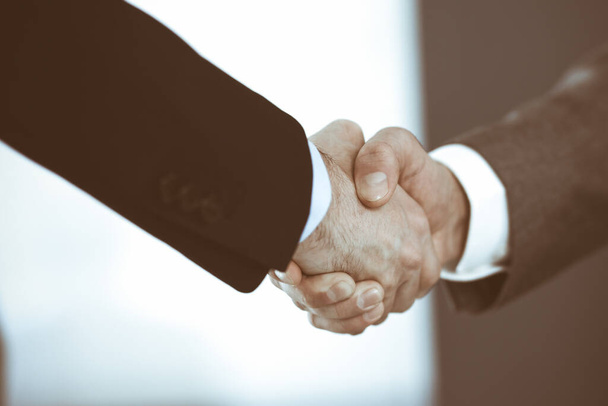 Business people shaking hands while standing with colleagues after meeting or negotiation, close-up. Group of unknown businessmen and women in modern office. Teamwork, partnership and handshake - Фото, зображення