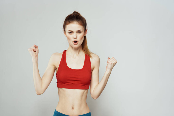 Uma mulher em uma camiseta vermelha em um fundo leve está envolvida em gestos de fitness com as mãos uma figura fina.  - Foto, Imagem