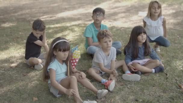Älykkäät monikansalliset lapset istuvat maassa puistossa oppitunnin aikana - Materiaali, video