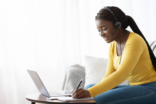 Imparare a distanza. Sorridente femmina africana in auricolare studiando con il computer portatile a casa - Foto, immagini