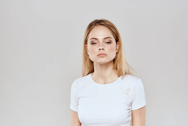cheerful blonde in a white t-shirt gesturing with her hands light background - Фото, изображение