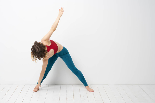Parlak bir odada spor yapan kadın yoga yapıyor. Mavi taytlı ve kırmızı kolsuz tişörtlü. - Fotoğraf, Görsel
