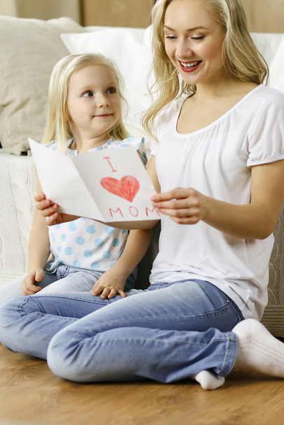Hyvää äitienpäivää. Lapsi tytär onnittelee äitiä ja antaa postikortin sydämen piirustuksella. Perheen ja lapsuuden käsitteet - Valokuva, kuva