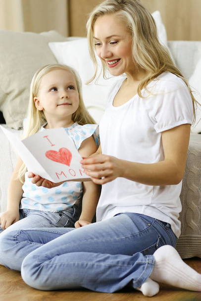 Happy mother day. Child daughter congratulates mom and gives her postcard with heart drawing. Family and childhood concepts - Фото, изображение