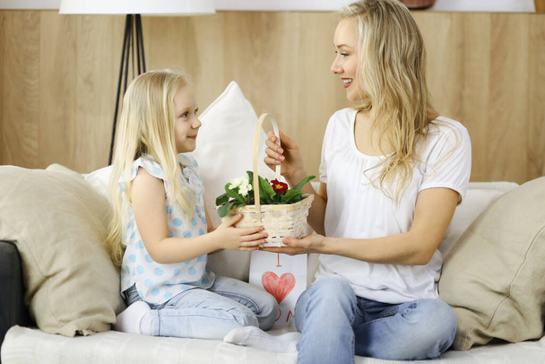 Happy mother day. Child daughter congratulates mom and gives her basket of spring flowers and postcard with heart drawing. Family and childhood concepts - Fotografie, Obrázek