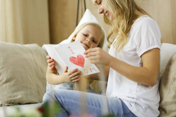 Happy mother day. Child daughter congratulates mom and gives her postcard with heart drawing. Family and childhood concepts - Zdjęcie, obraz