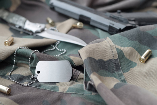 Leger Dog tag token met 9mm kogels en pistool liggen op gevouwen camouflage groene stof. Een set van militaire veteranen items of oude plicht trofee kit - Foto, afbeelding