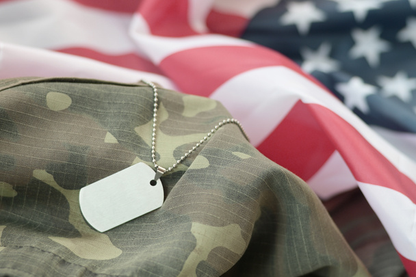 Zilverkleurige militaire kralen met hondenlabel op Amerikaanse stoffen vlag en camouflage uniform. Leger symbool op USA banner close-up. Memorial day concept - Foto, afbeelding