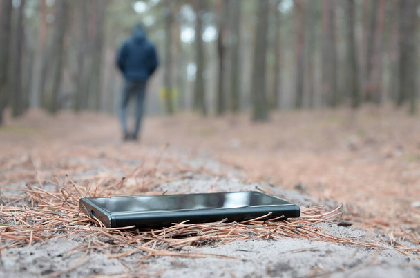 Niño pierde su teléfono inteligente en el camino de madera de abeto de otoño ruso. Descuidado y pérdida de costoso concepto de dispositivo móvil - Foto, imagen