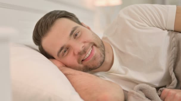 Portrait de jeune homme allongé au lit souriant à la caméra  - Séquence, vidéo