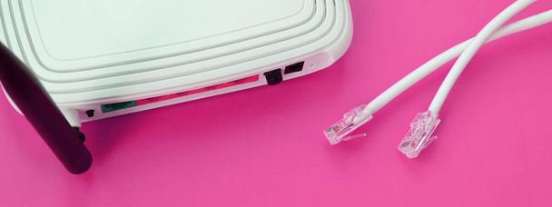 Маршрутизатор и подключаемые к Интернету кабельные розетки лежат на ярко-розовом фоне. Элементы, необходимые для подключения к Интернету - Фото, изображение