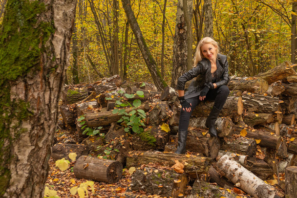 In the forest, a girl stands in a leather jacket and black jeans. Beautiful with a kind look - Foto, afbeelding