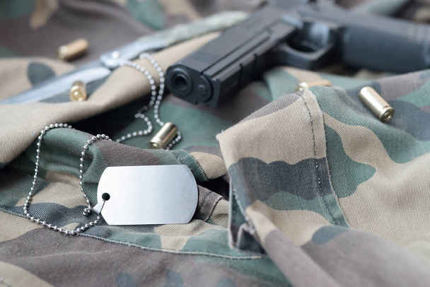 Жетон Army Dog с 9-миллиметровыми пулями и пистолетом лежит на сложенной камуфляжной зеленой ткани. Набор предметов для ветеранов войны или старый набор для трофеев - Фото, изображение