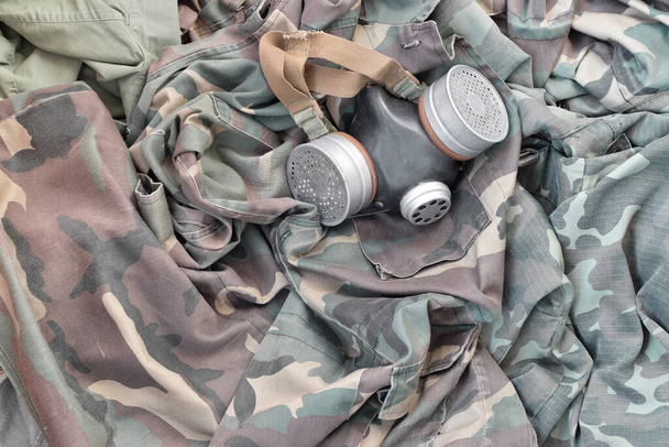 Stalker soldiers soviet gas mask lies on many green khaki camouflage jackets. Post apocalypse surviving concept - Photo, Image
