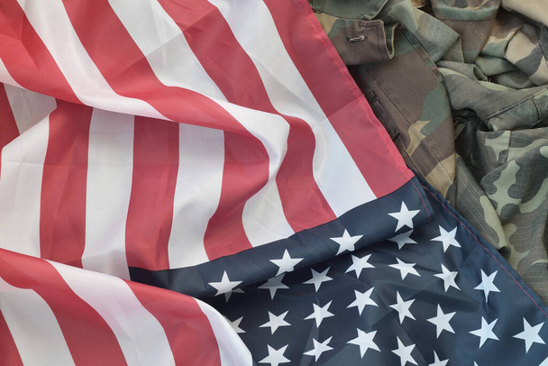 Σημαία Ηνωμένων Πολιτειών Αμερικής και διπλωμένο στρατιωτικό σακάκι. Στρατιωτικά σύμβολα εννοιολογικό πανό υπόβαθρο για την αμερικανική πατριωτικό σχεδιασμό διακοπών - Φωτογραφία, εικόνα