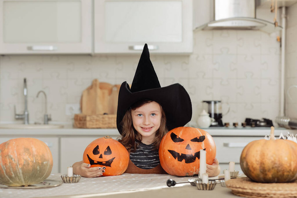 Fijne Halloween. Schattig klein meisje in heksenkostuum met gesneden pompoen. gelukkig familie voorbereiding voor Halloween - Foto, afbeelding