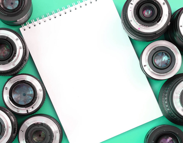 Useat valokuvauslinssit ja valkoinen muistikirja ovat kirkkaalla turkoosilla taustalla. Tekstitila - Valokuva, kuva