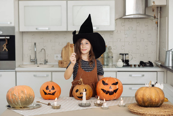 Счастливого Хэллоуина. Милая маленькая девочка в костюме ведьмы с вырезанной тыквой. Счастливая семья готовится к Хэллоуину. девушка зажигает свечи. - Фото, изображение