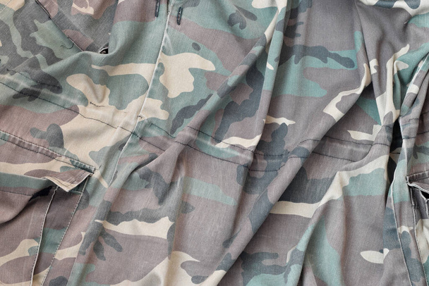 Camouflage background texture as backdrop for hunting or fishing design projects. Back side of hunters camouflage jacket with many pleats on crumpled fabric - 写真・画像