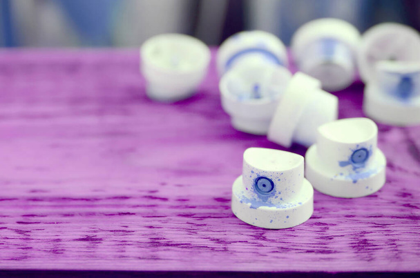 Las boquillas azules sucias del pulverizador de pintura se encuentran sobre una plancha púrpura sobre un fondo de muchas latas sucias para pintar graffiti - Foto, Imagen