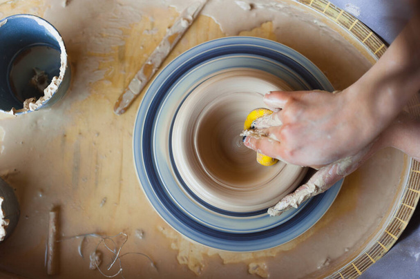 女の子の陶芸家は、ぬれた黄色のスポンジ、写真のクローズアップトップビューを使用して出版物で動作します. - 写真・画像