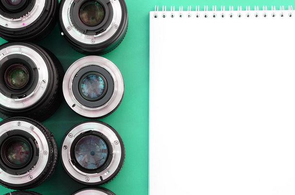 Verschillende fotografische lenzen en een wit notitieboekje liggen op een helderturquoise achtergrond. Ruimte voor tekst - Foto, afbeelding