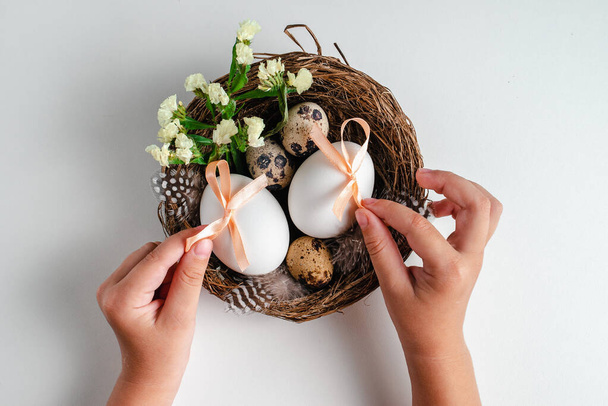 Young woman holding Easter eggs and flowers in  nest on white background. Greeting card - 写真・画像