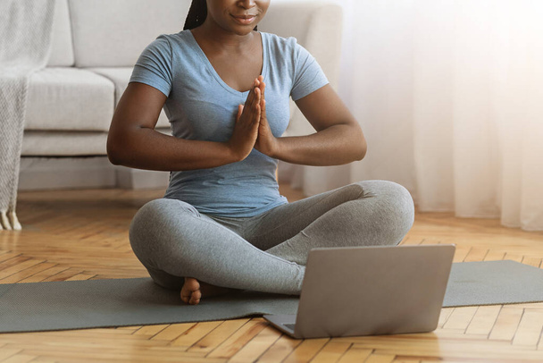 Černá dáma medituje doma, sedí na podložce před laptopem - Fotografie, Obrázek