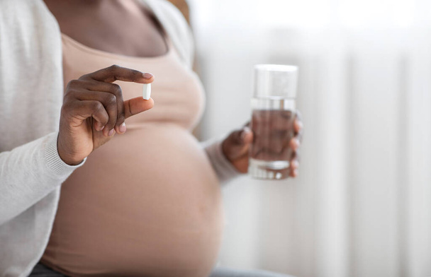 Suplementos durante a gravidez. Pílula Expectante Preta Ireconhecível Senhora Segurando E Vidro De Água - Foto, Imagem