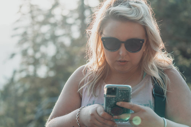 Serieuze vrouw met een zonnebril gebruikt mobiele telefoon terwijl buiten, op zoek naar bezorgd - Foto, afbeelding