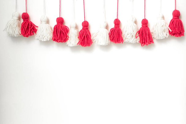 brushes from yarn of red and white color on a white background. Space for copy space. DIY yarn brushes. Garland. Garland of yarn. Pampushki from yarn. Children's creativity - Foto, afbeelding