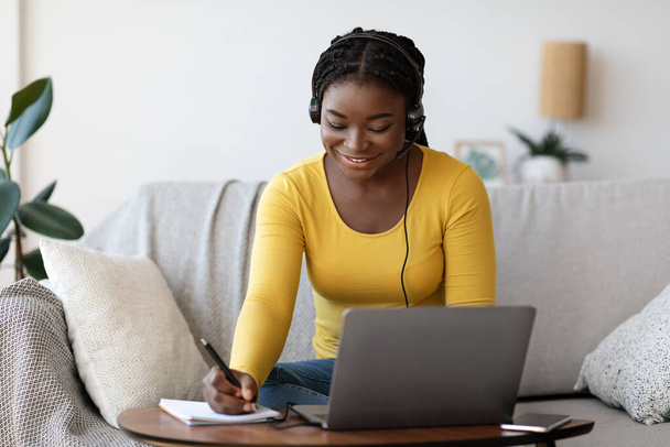 Educación en línea. Mujer negra sonriente en auriculares que estudia con el ordenador portátil en casa - Foto, imagen