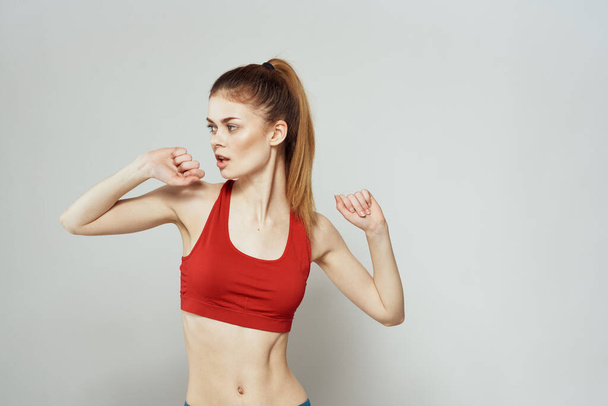 Una mujer con una camiseta roja sobre un fondo claro se dedica a gestos de fitness con las manos una figura delgada  - Foto, imagen