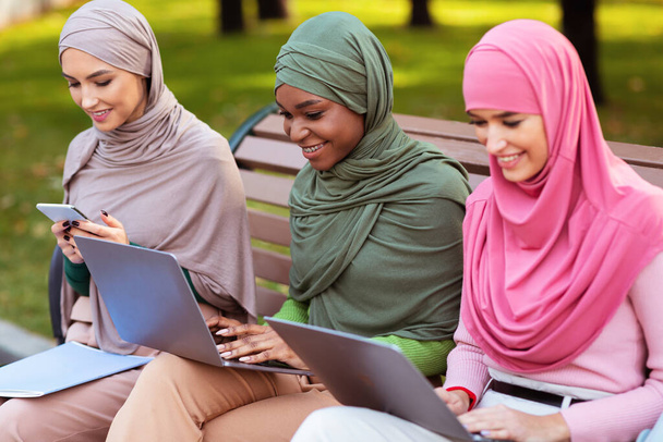 Muslimi opiskelijat Naiset käyttävät vempaimia Learning Online istuu puistossa - Valokuva, kuva
