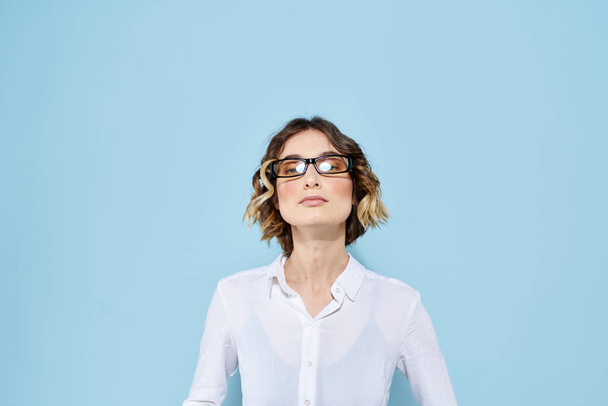Femme d'affaires sur un fond bleu lunettes avec des jantes sombres cheveux bouclés Chemise légère vue recadrée - Photo, image