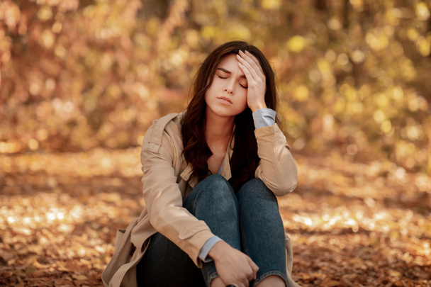 Jeune femme fatiguée ou déprimée touchant la tête au parc d'automne - Photo, image