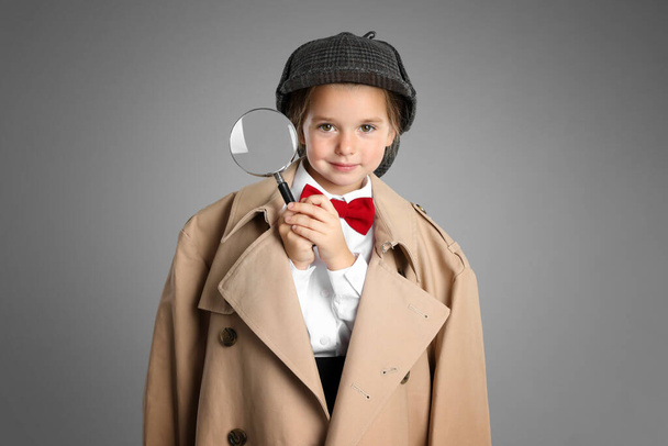 Cute little child in hat with magnifying glass playing detective on grey background - Foto, Imagem