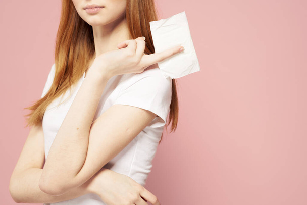 Red-haired woman with a pad in her hand and in a white T-shirt on a pink background hygiene care for the appearance - Photo, Image