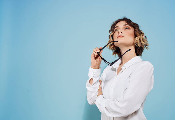 Woman model in white shirt on a blue background holds glasses in her hand - Foto, Imagem