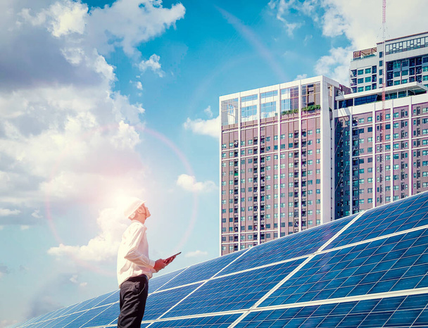 Un ingeniero se paró en una planta de energía solar y en su mano sostuvo un portátil, Miró el edificio alto para analizar algo. Energía alternativa para conservar la energía del mundo en el futuro. - Foto, imagen