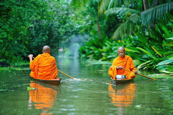 Buddhist monk in small wooden boat rowing in canal to receive food from villagers in morning, Buddhist monk in wooden boat in canal at Takha flaoting market, popular tourist attraction in Thailand - Photo, image