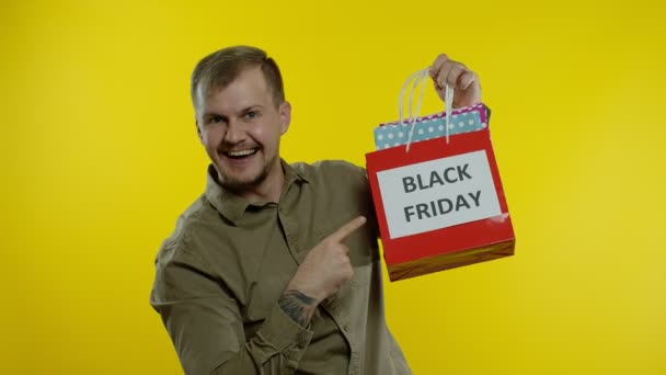 Homem mostrando inscrição Black Friday em sacos de compras, sorrindo, satisfeito com compras de preços baixos - Filmagem, Vídeo